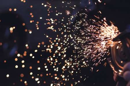 Bright sparks fanning out from an angle grinder against a dark workshop background with bokeh lights.