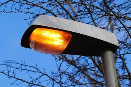 Close-up of an LED street light head glowing amber against a blue dusk sky.